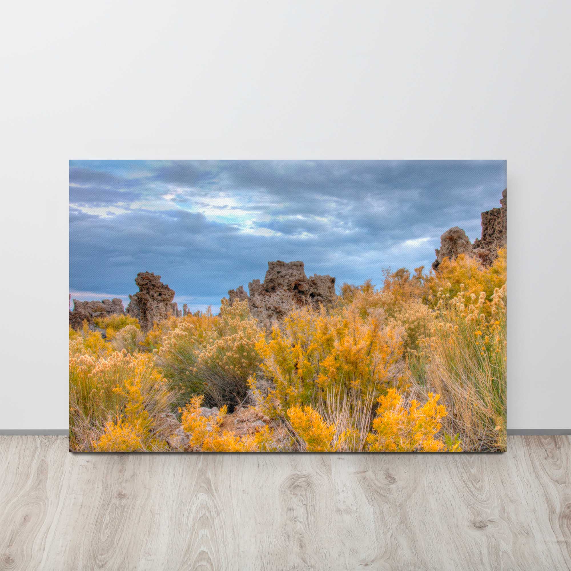 Canvas print of a desert landscape with yellow bushes and rocky formations under a cloudy sky.