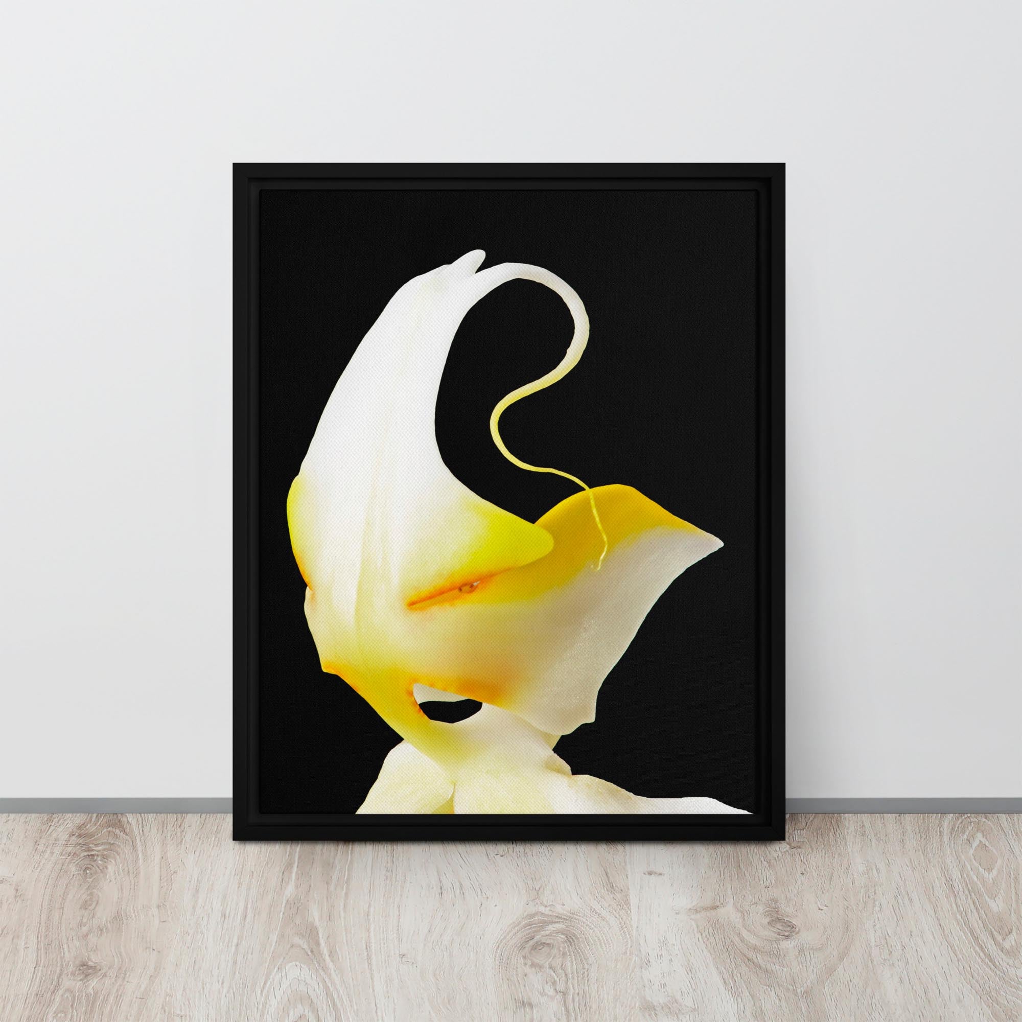 Framed photograph of a yellow flower against a black background on a light wood floor.