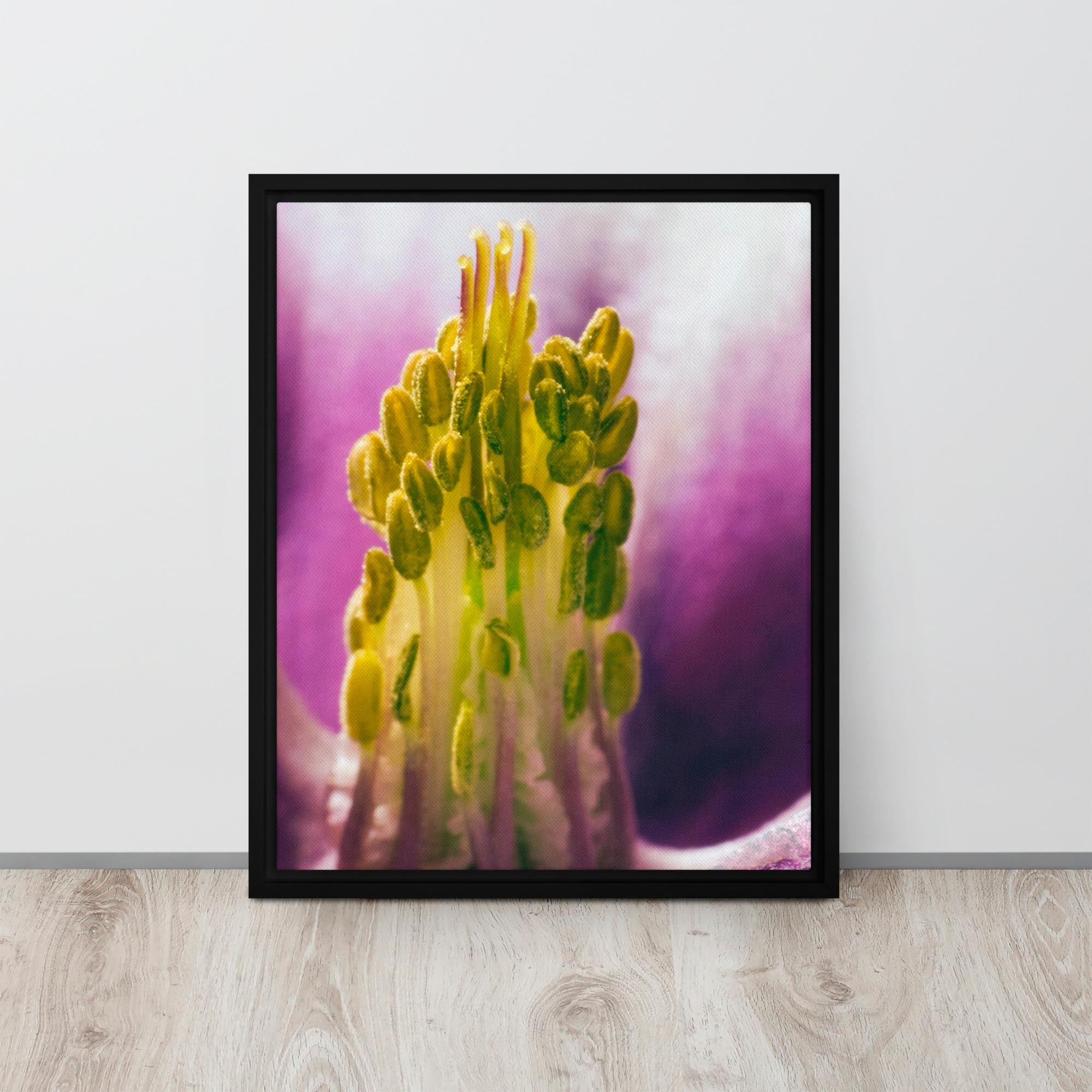 Framed photograph of a yellow flower with a purple background on a white wall.